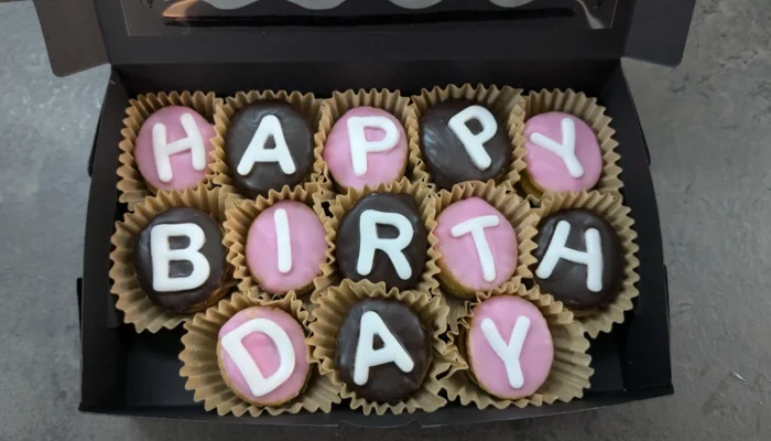 Eine Schachte mit dreizehn glasierten Keksen in Förmchen angeordnet zu dem Wort "HappyBirthday"