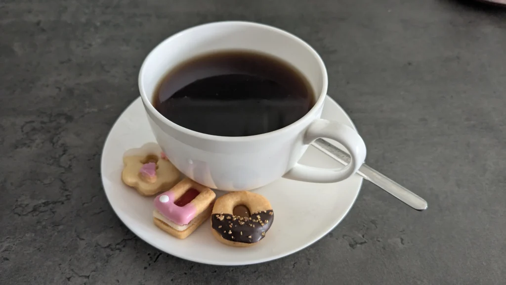 Eine Tasse Kaffee mit einem Teelöffel auf einer Untertasse mit 3 verschiedenen Plätzchensorten
