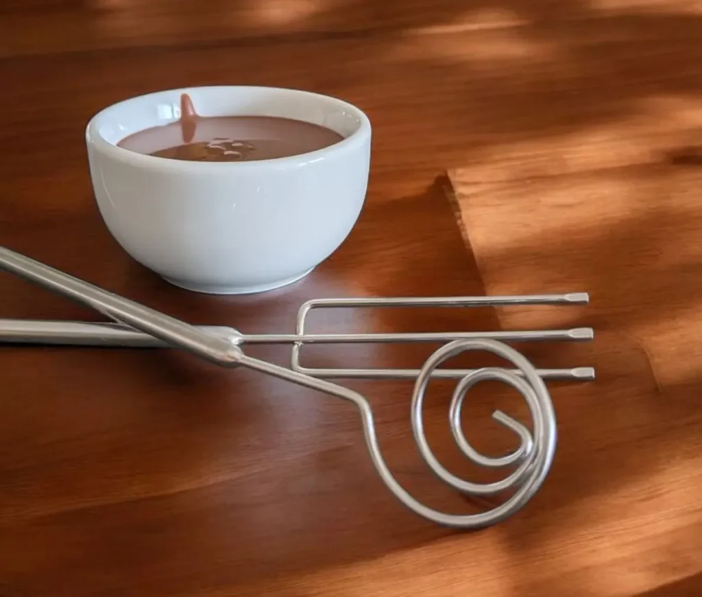 Eine Schüssel mit Schokoladenglasur auf einer Holzunterlage und daneben Glasurutensilien